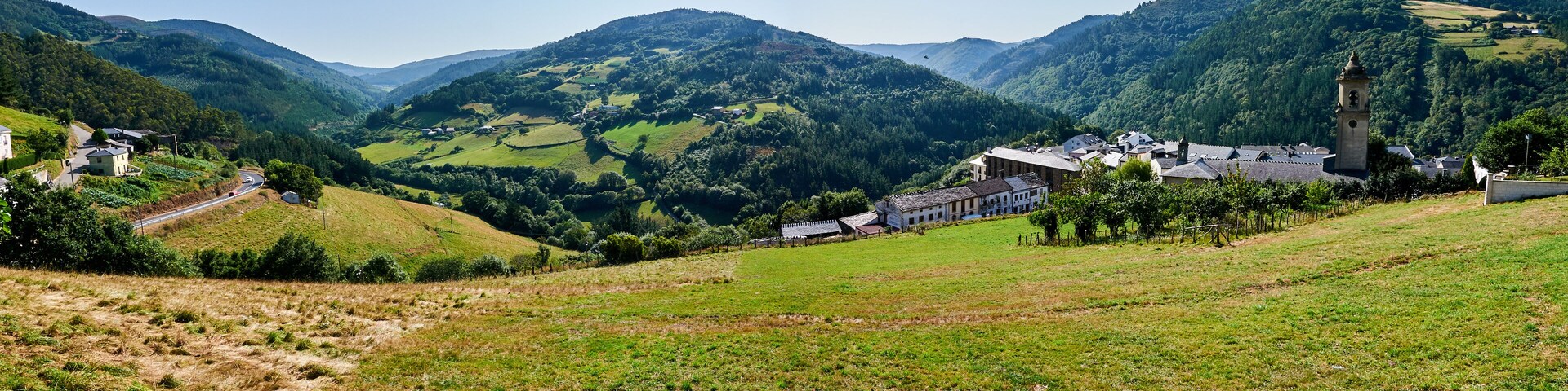 Um vale com uma pequena aldeia, campos verdes e montanhas ao fundo.