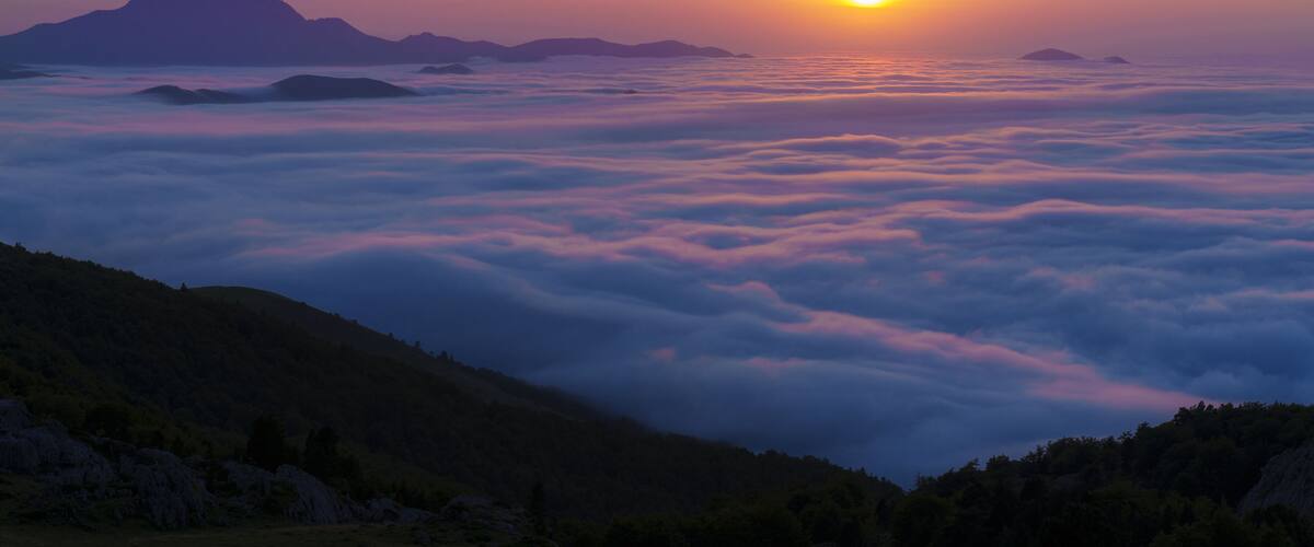 A sunrise over a mountain range with clouds below.