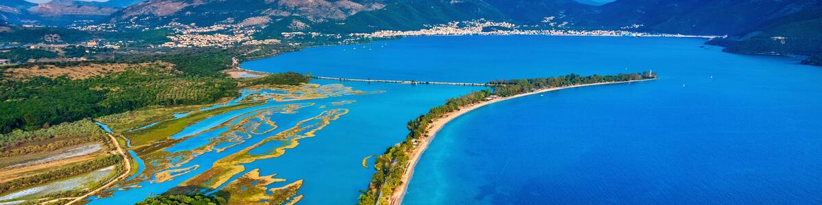 Une vue aérienne d’un paysage côtier, avec une route sinueuse, des eaux d’un bleu limpide et une ville située au loin.