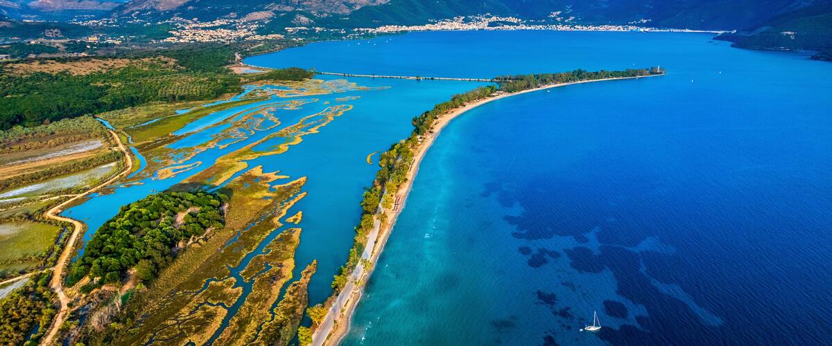 An aerial view of a coastal landscape with a curving road, clear blue waters, and a distant town.