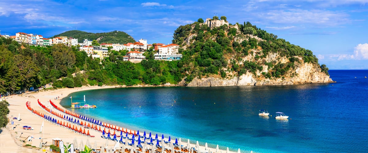A coastal town with a beach, a castle on a hill, and boats on the water.