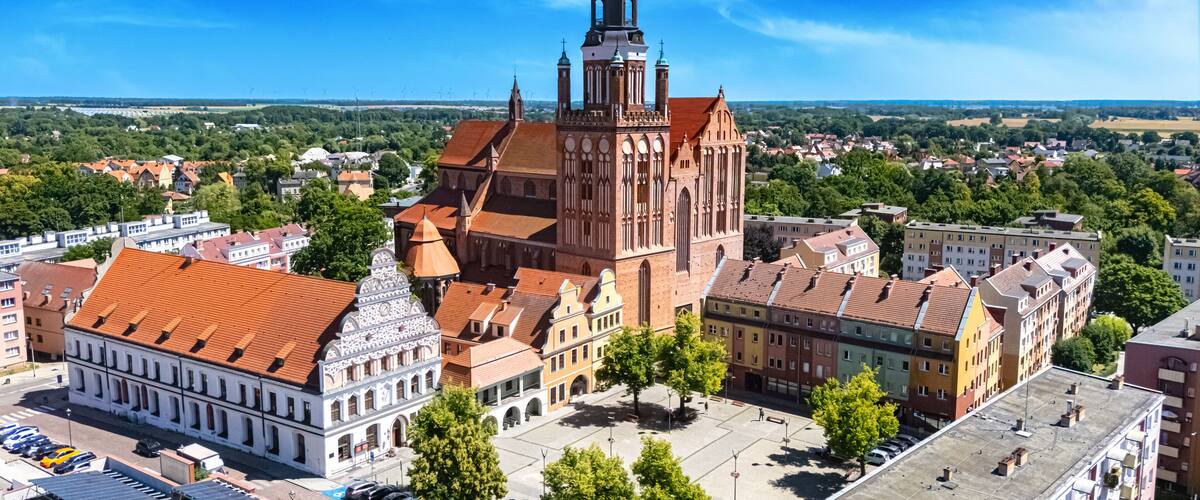 A historic church with a tall tower and a red-tiled roof, surrounded by colorful buildings and a clear blue sky.