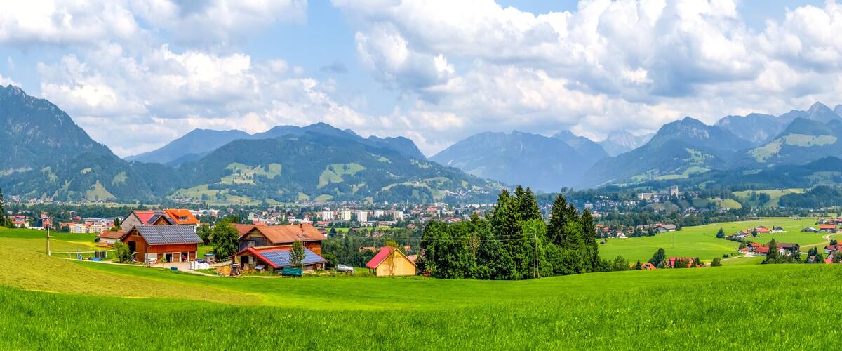 A mountainous landscape with a village, green fields, and a prominent peak in the background.