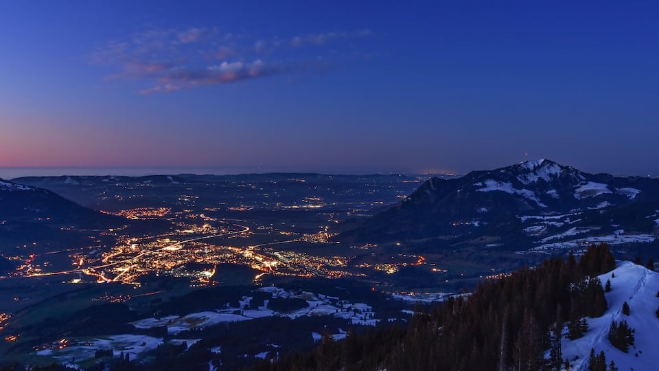 City night lights of Sonthofen (Allgaeu, Bavaria, Germany) after sunset with Gruenten mountain in winter. Landscape in twilight with blue sky and some clouds.