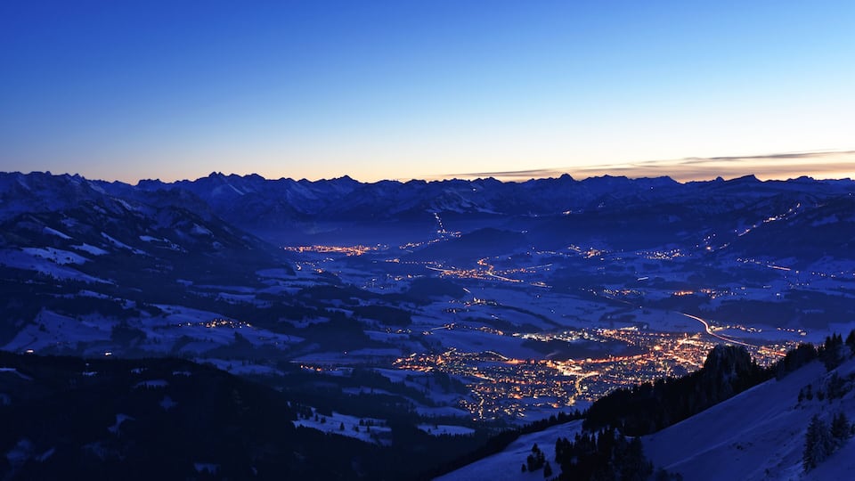 City night lights of Sonthofen and Oberstdorf (Allgaeu Alps, Bavaria, Germany) after sunset from the summit of Gruenten mountain in winter. Alpine landscape during blue hour. Copy space.