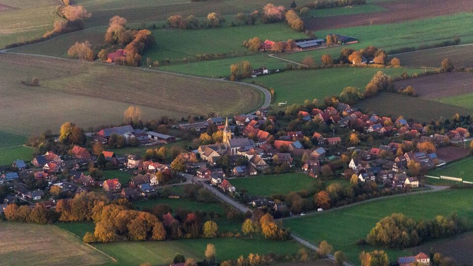 An aerial view of a rural village with houses, fields, and a church.