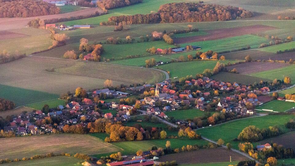 An aerial view of a small town with a church, surrounded by fields and trees.