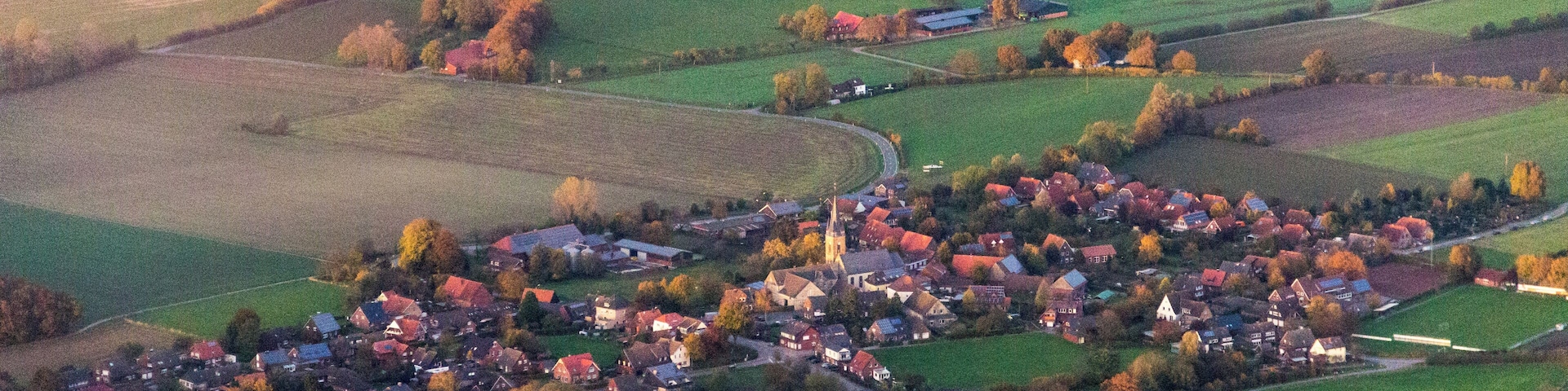 An aerial view of a small town with a church, surrounded by fields and trees.
