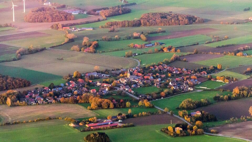 An aerial view of a rural village with wind turbines, fields, and scattered houses.