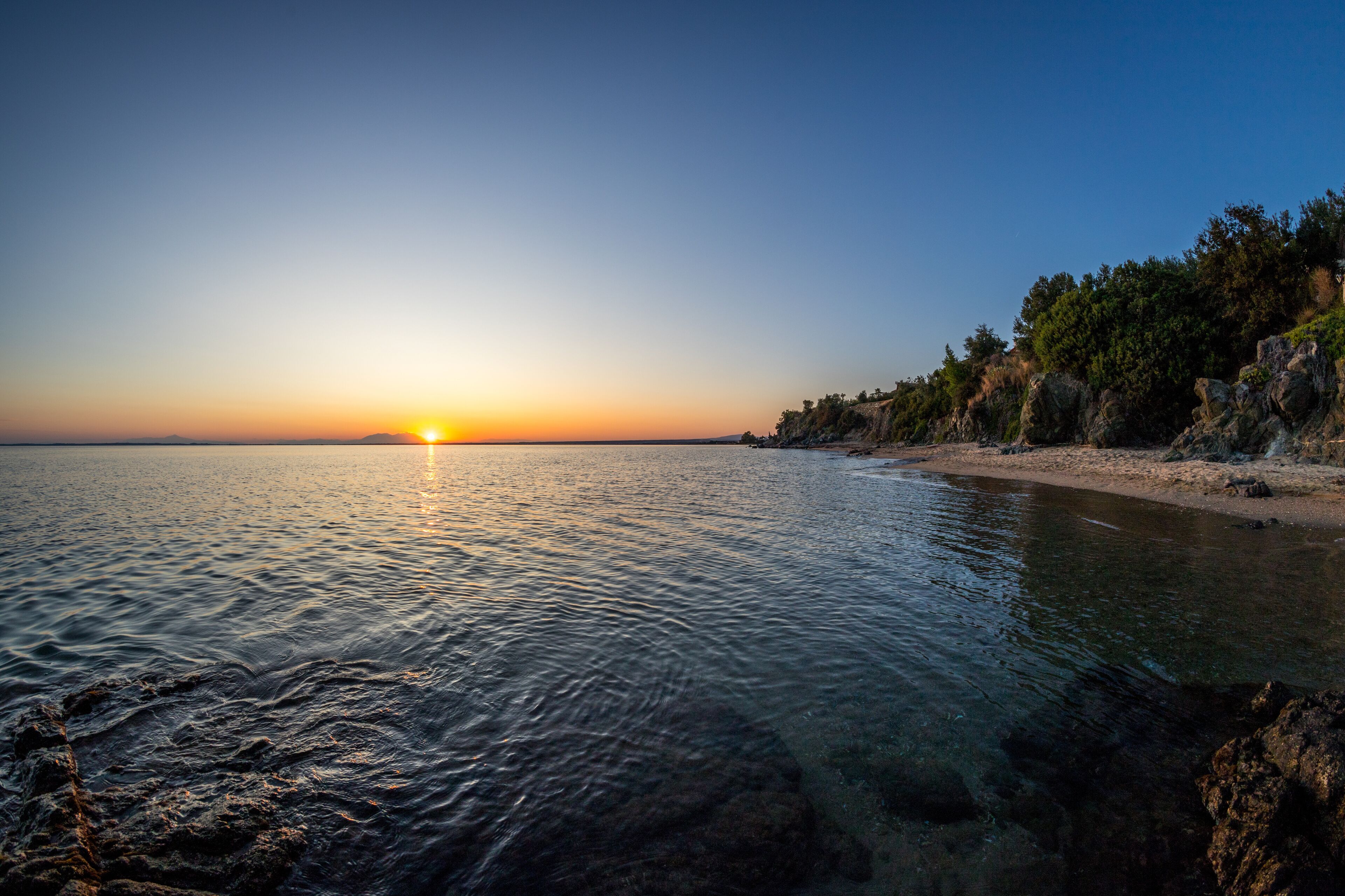 A sunset over a calm sea with rocky cliffs and a sandy beach.
