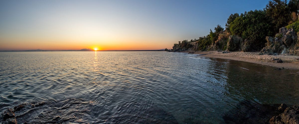 A sunset over a calm sea with rocky cliffs and a sandy beach.