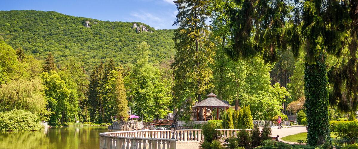 A serene lake surrounded by lush greenery, a gazebo, and a stone bridge.