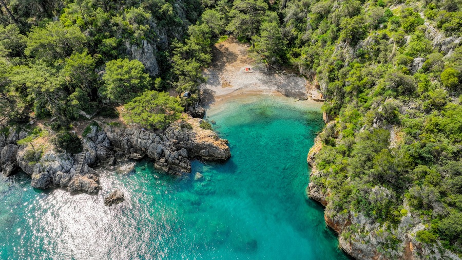 Una cala turquesa rodeada de acantilados rocosos y densa vegetación verde.