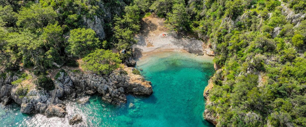 A turquoise bay surrounded by rocky cliffs and dense green foliage.