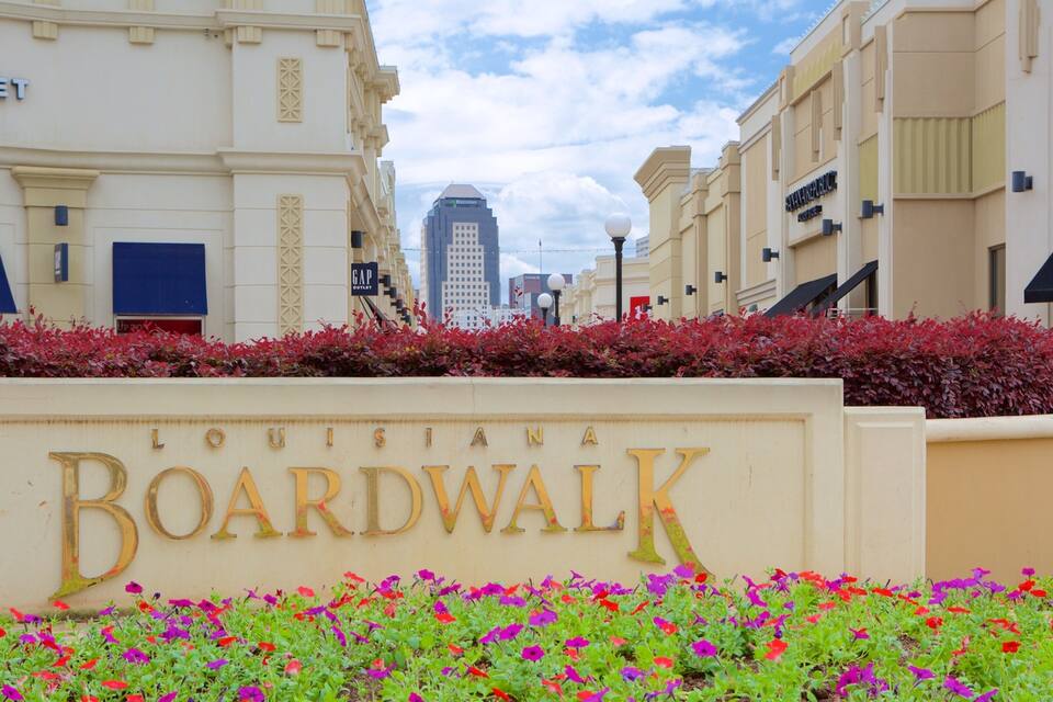 Placa indicando 'Louisiana Boardwalk' com flores coloridas em frente.