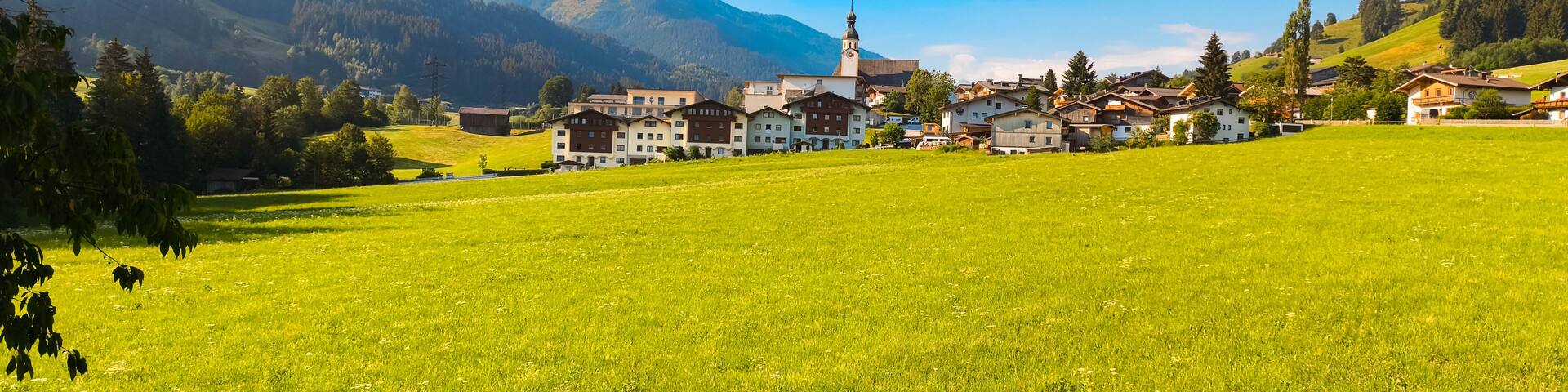 A green field, a church with a tower, and mountains in the background.