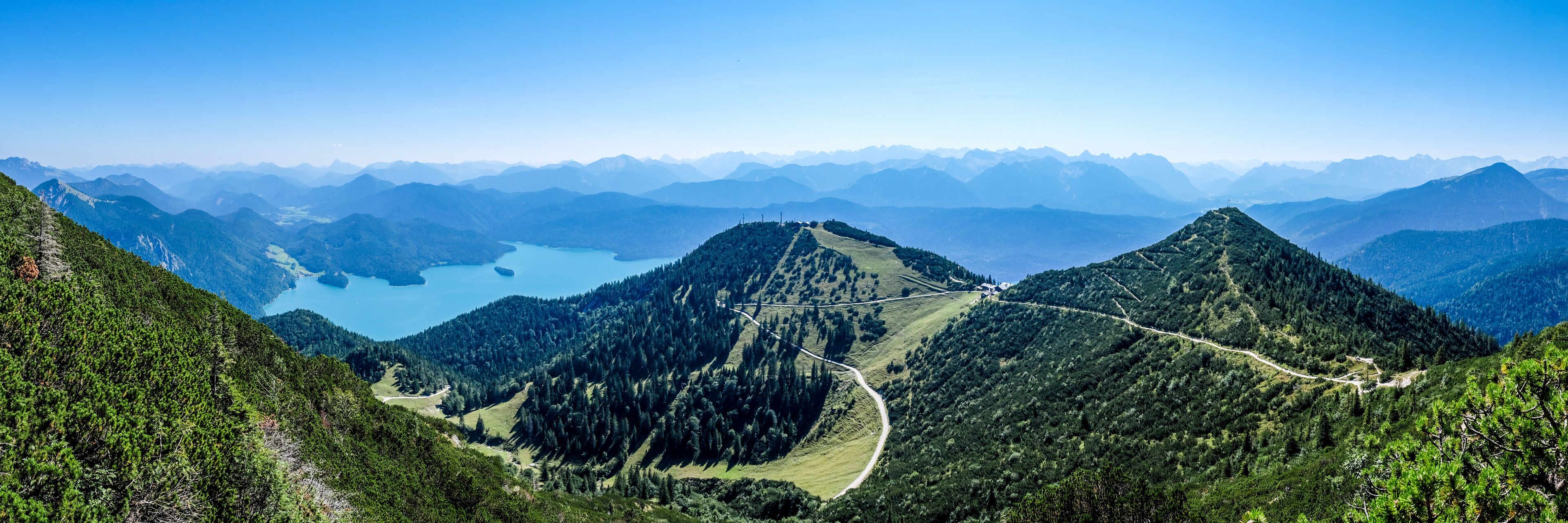 A mountain landscape with a winding road, dense forests, and a lake.
