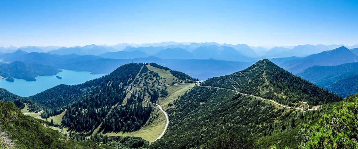A mountain landscape with a winding road, dense forests, and a lake.