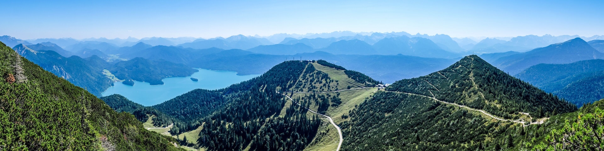 A mountain landscape with a winding road, dense forests, and a lake.