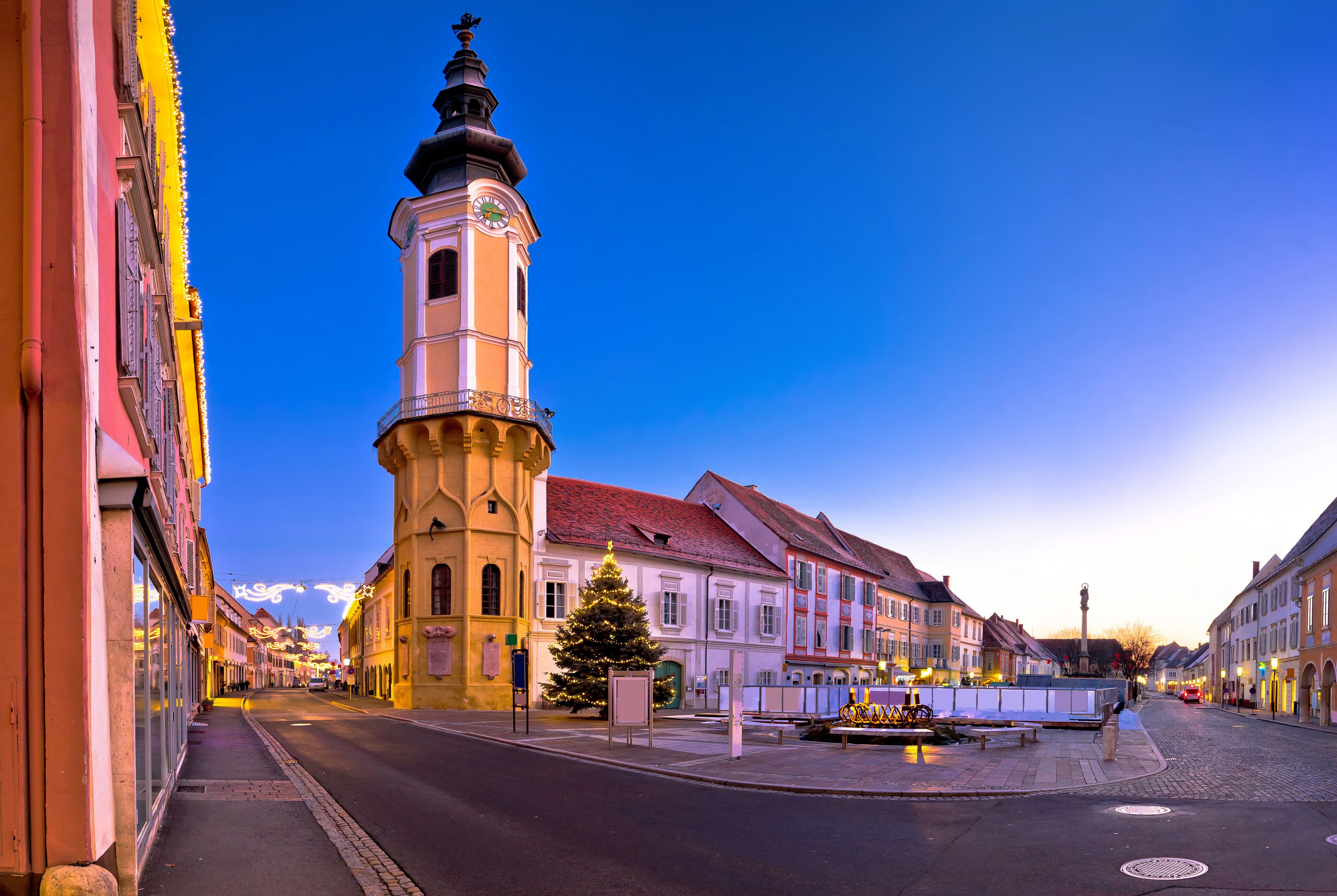 A street with a clock tower, a Christmas tree, and traditional European architecture.