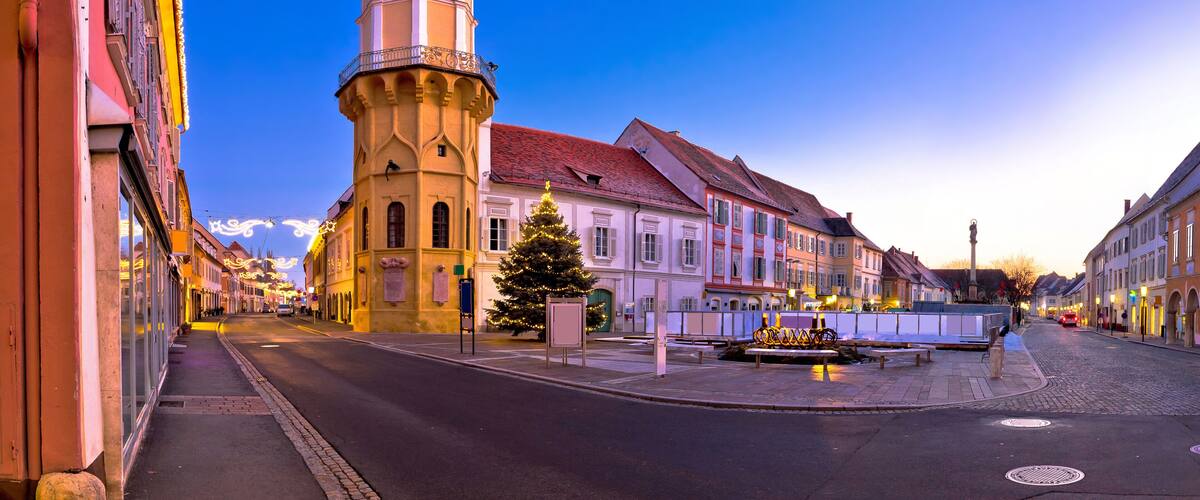 A street with a clock tower, a Christmas tree, and traditional European architecture.
