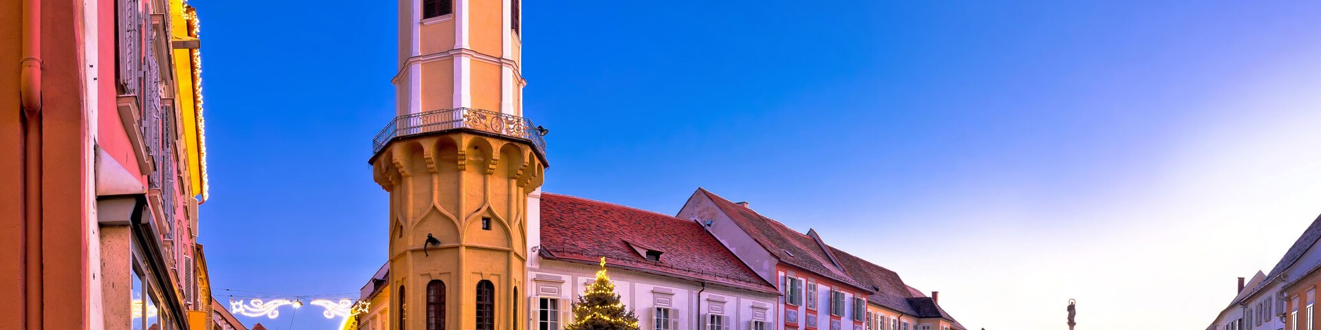 A street with a clock tower, a Christmas tree, and traditional European architecture.