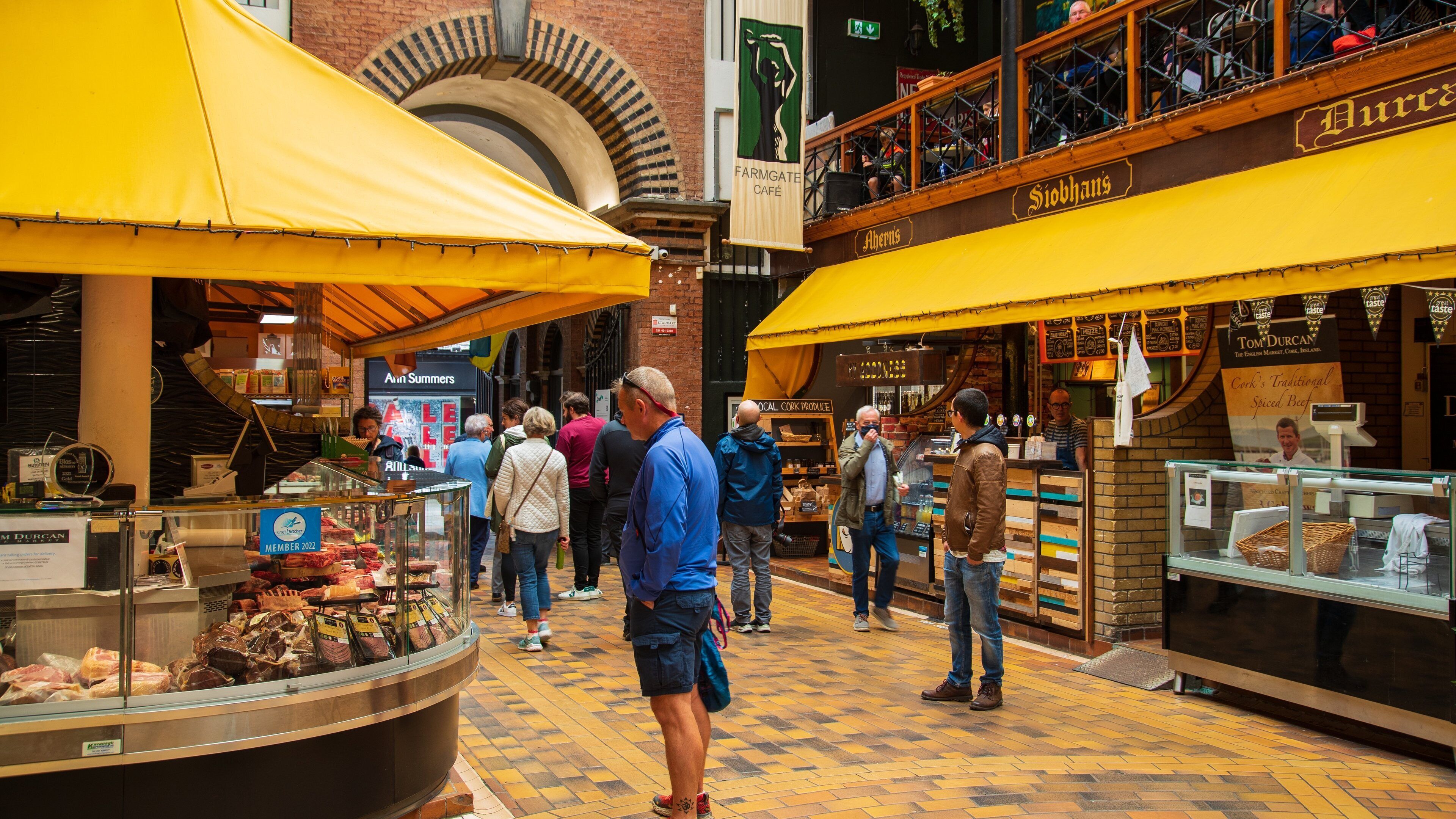 A bustling indoor market with yellow canopies, a butcher shop, and a sign for Tom Durcan.