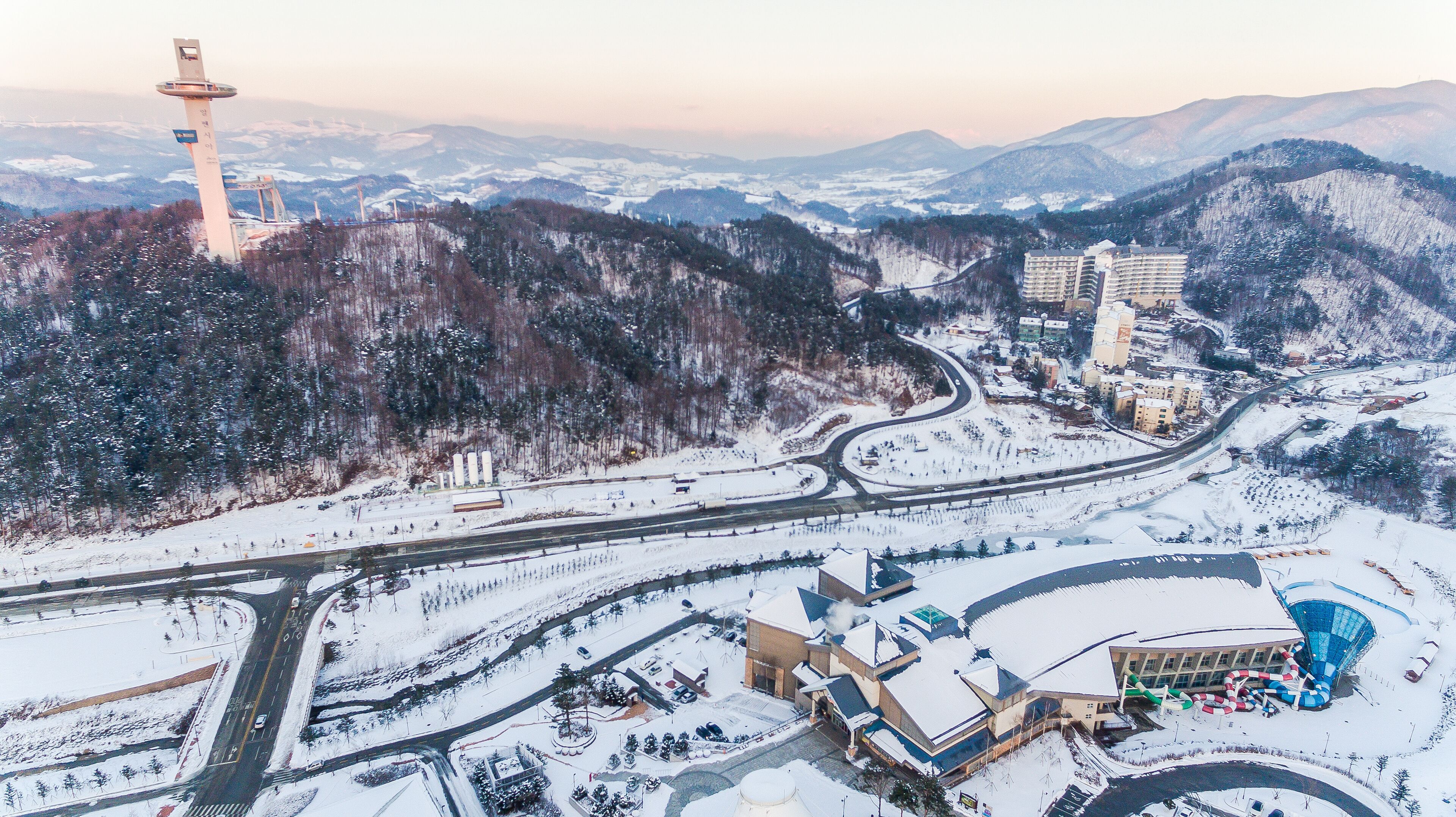 A snowy landscape with a tower, roads, buildings, and a ski resort.