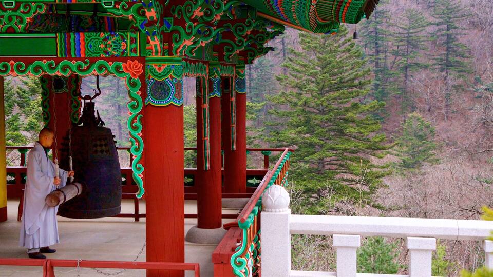 A traditional structure with ornate red and green decorations, a large bell, and a person in traditional attire.