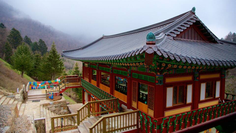 A traditional Korean building with a tiled roof and colorful decorations, surrounded by a mountainous landscape.
