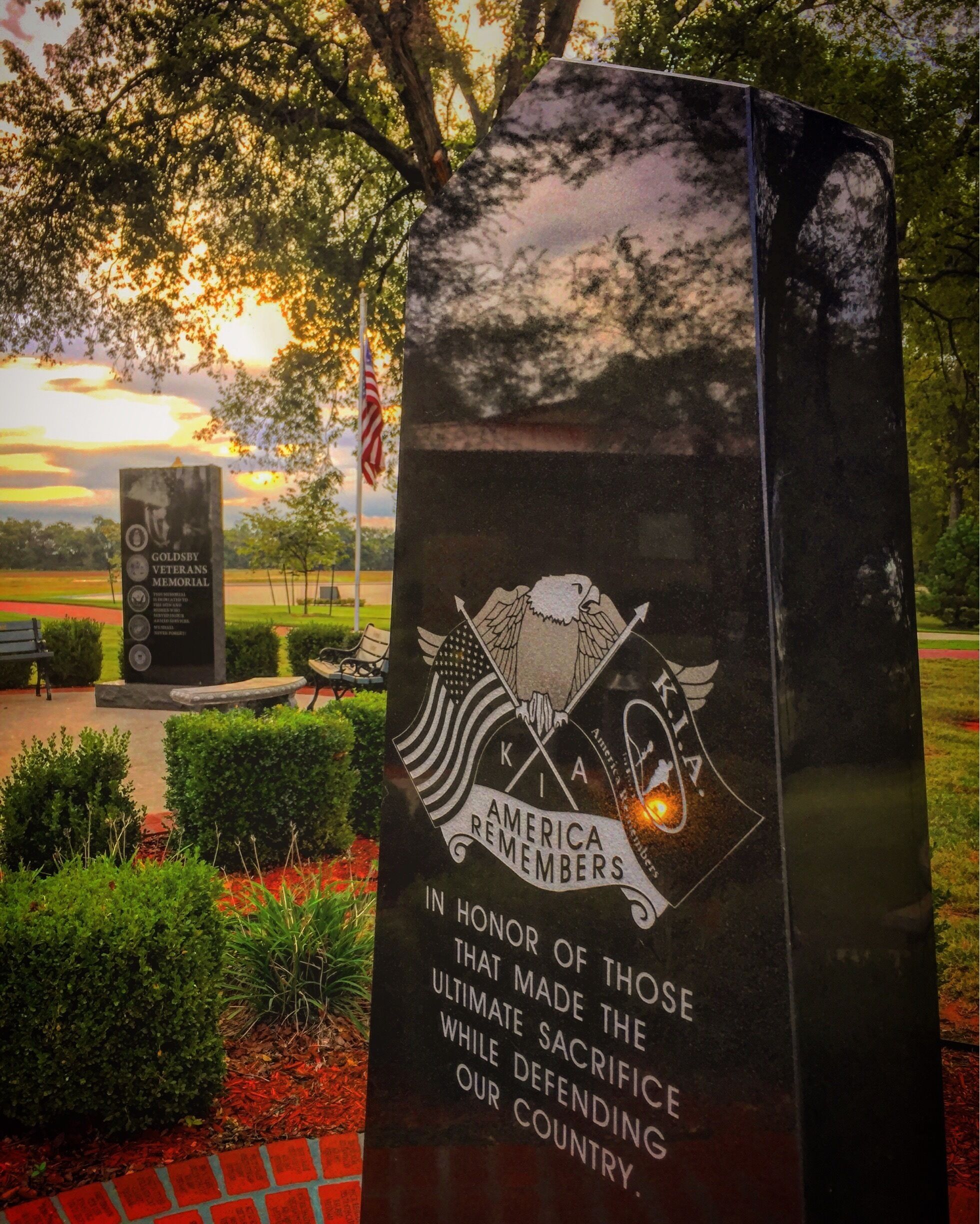 A memorial with an eagle and a flag, surrounded by greenery and a sunset in the background.