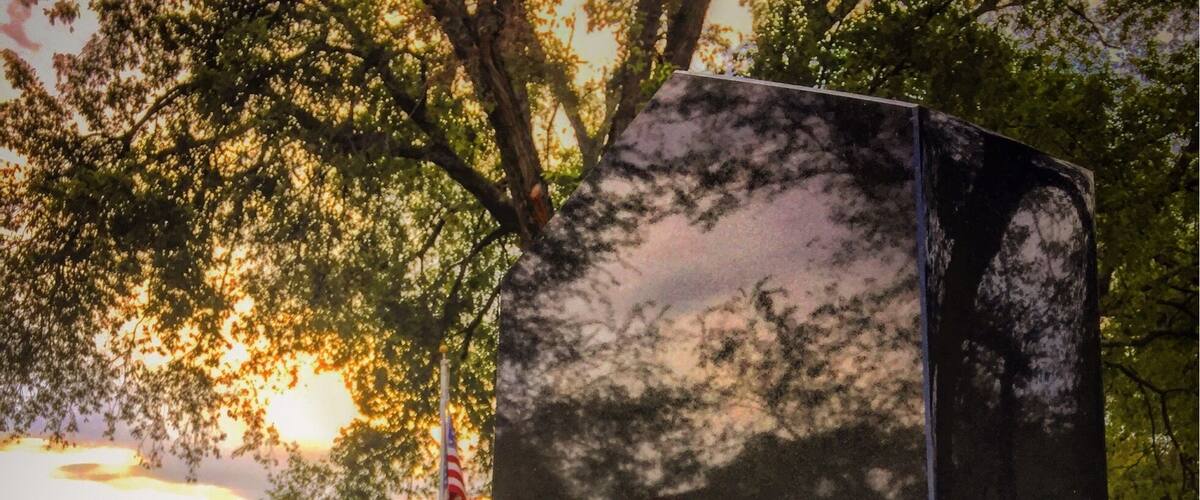 A memorial with an eagle and a flag, surrounded by greenery and a sunset in the background.