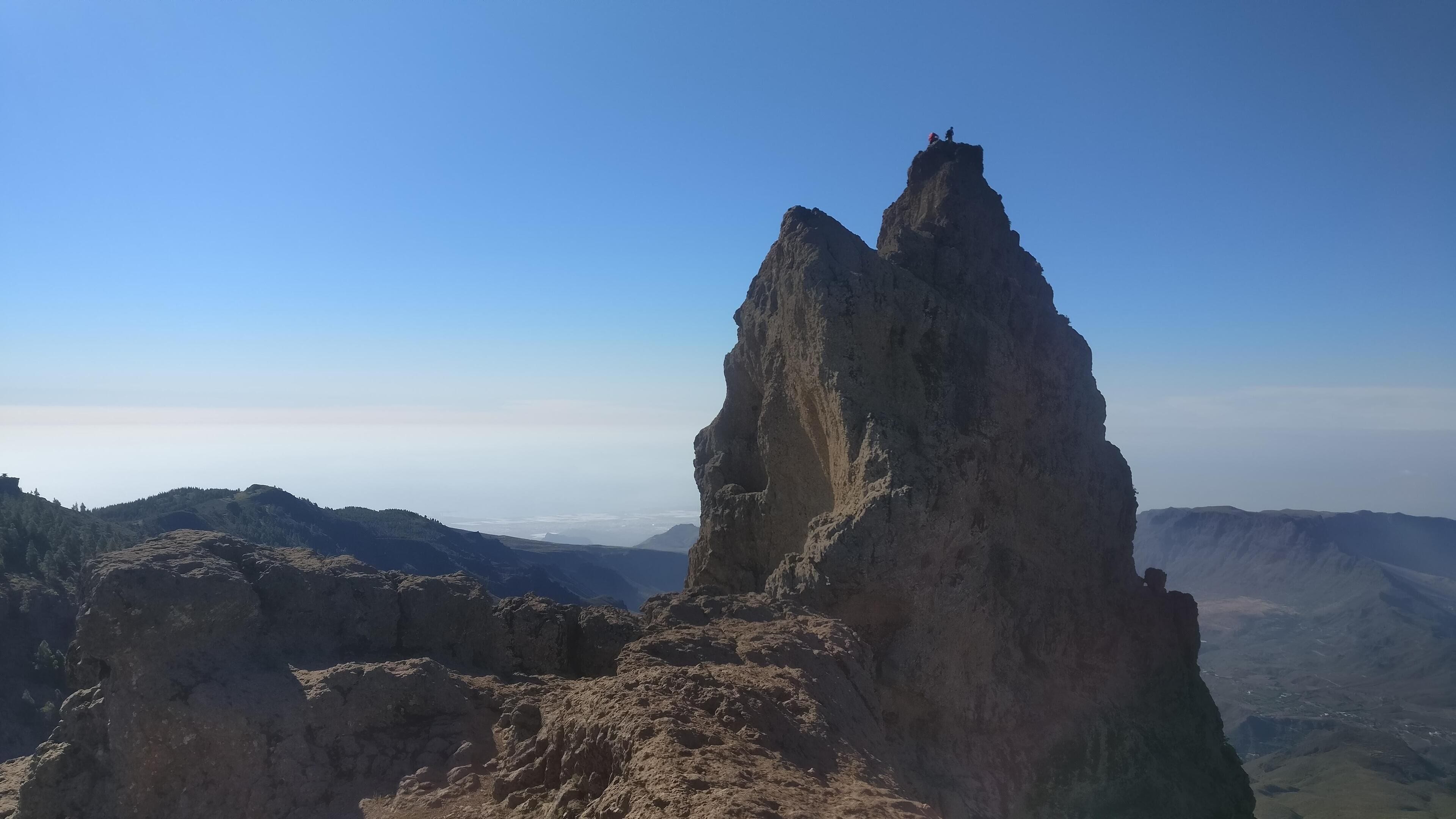 Ett kargt bergstopp med två klättrare på toppen.