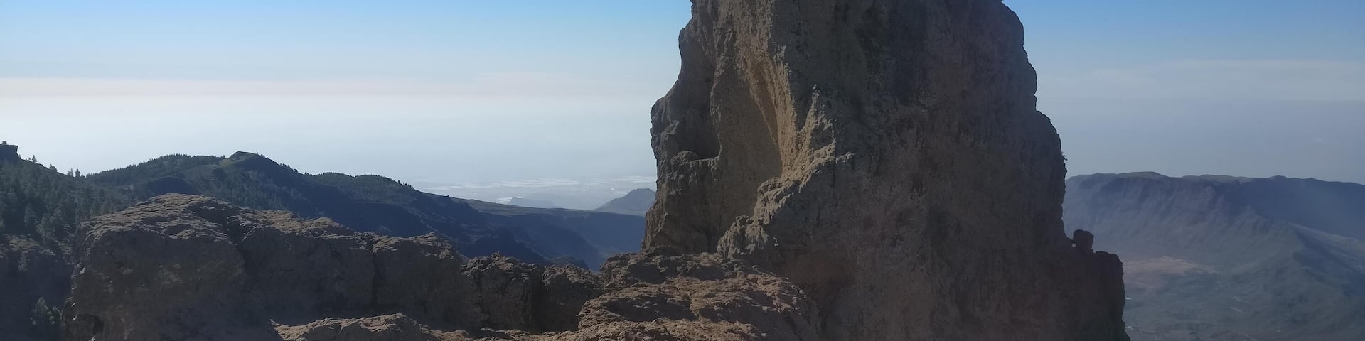 A rugged mountain peak with two climbers at the summit.
