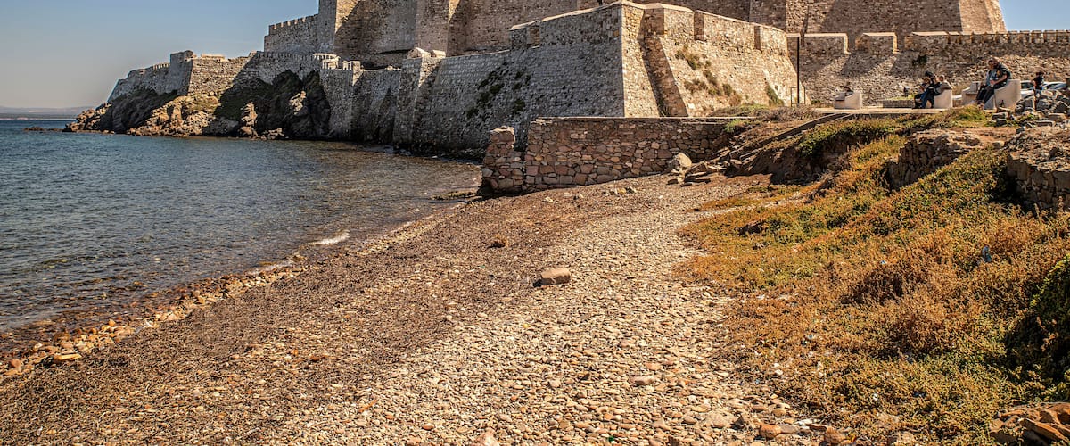 A historic stone castle by a rocky shoreline.