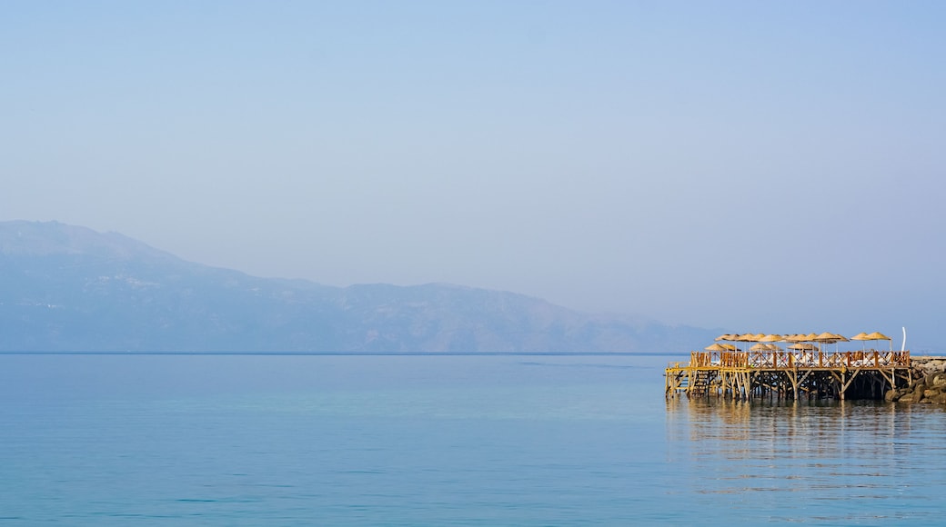 A calm sea with a wooden pier extending into it, surrounded by mountains in the background.
