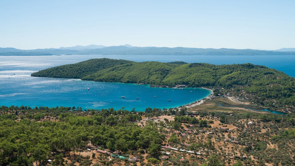 A coastal landscape with a forested island, clear blue waters, and a small settlement.