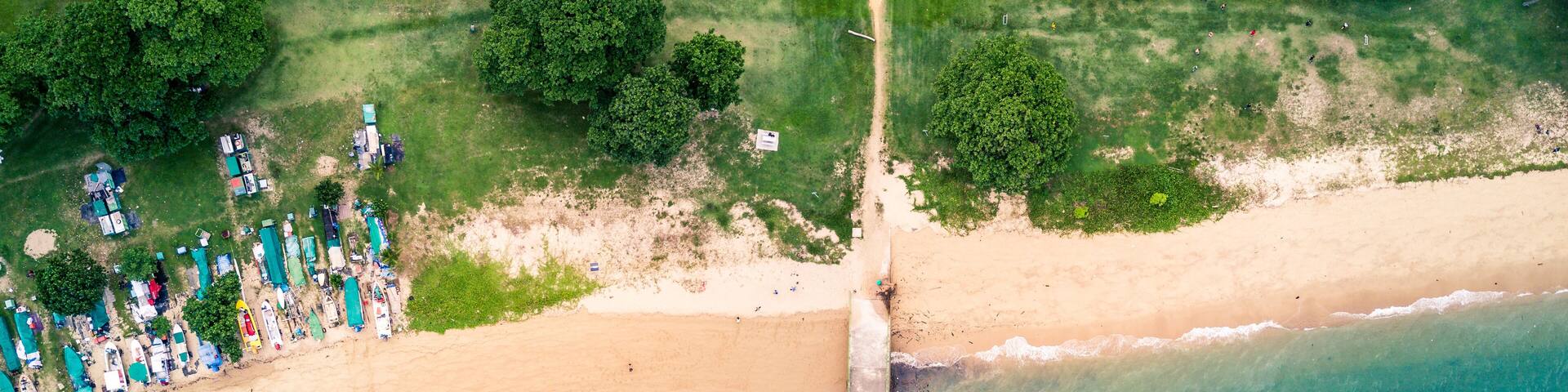 An aerial view of a beach with a pier extending into the water, surrounded by greenery and beachgoers.