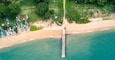 An aerial view of a beach with a pier extending into the water, surrounded by greenery and beachgoers.