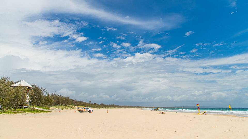 A beach with a white building, a white truck, and a lifeguard flag.