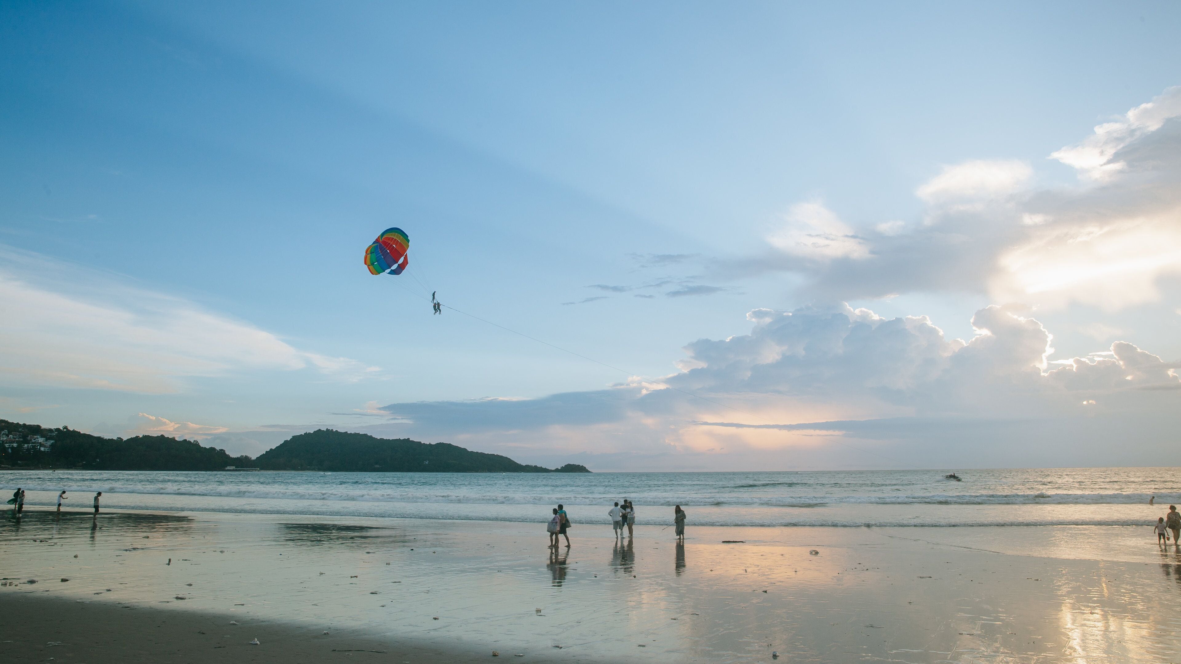 A beach with people walking and a colorful kite flying.
