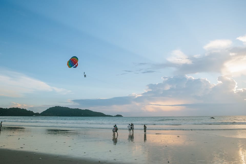 Uma praia com pessoas caminhando e um colorido pipa voando.