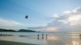 Une plage où l’on voit des gens se promener et un cerf-volant coloré dans le ciel.