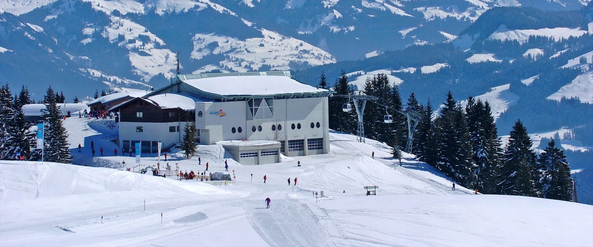 A ski resort with a building, ski slopes, and snow-covered mountains in the background.