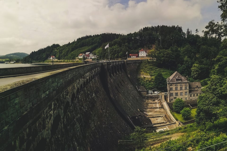 A large dam with a lock system, surrounded by lush greenery and a small village with traditional buildings.