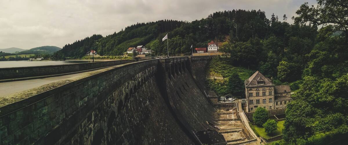 A large dam with a lock system, surrounded by lush greenery and a small village with traditional buildings.