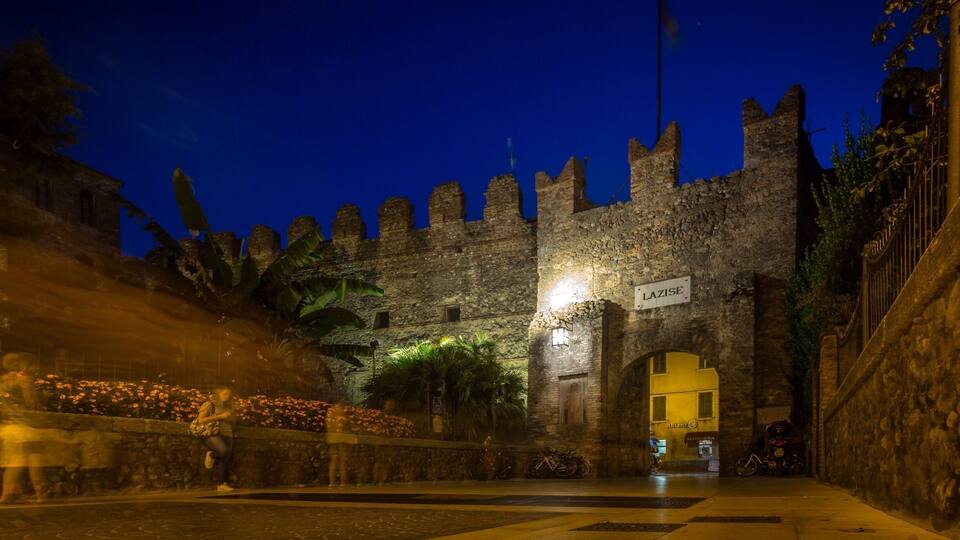 A historic stone gate with a sign reading "LAZISE" at night.
