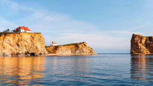 A coastal landscape with a house on a cliff and a prominent rock formation in the water.