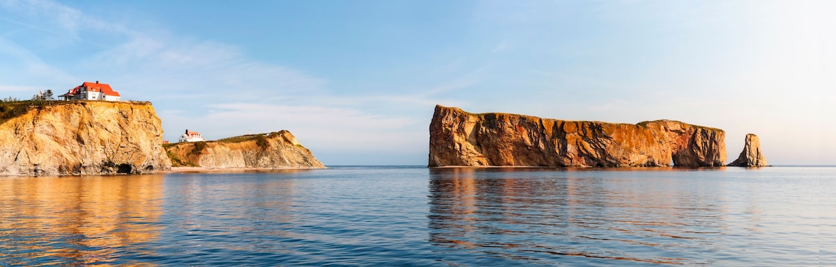 A coastal landscape with a house on a cliff and a prominent rock formation in the water.