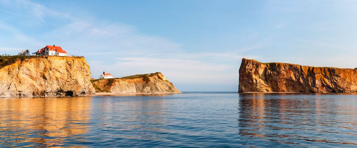 A coastal landscape with a house on a cliff and a prominent rock formation in the water.